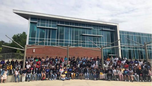 A large group of 156 students from the 32nd Street Theater HBCU tour posing in front of Fort Valley State University's modern glass-fronted building.