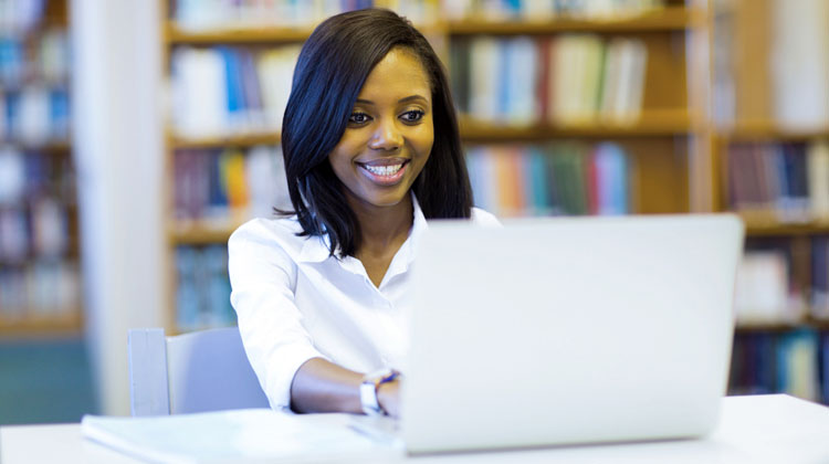 African American senior submits her college application online at the school library.