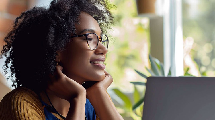 Smiling young woman with curly hair wearing glasses, looking away thoughtfully in front of a laptop while exploring a list of professional certifications.