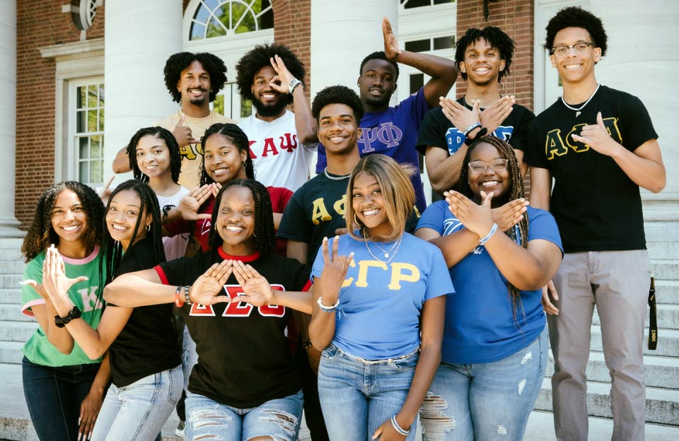 A diverse group of HBCU students proudly displaying hand signs and letters representing their black fraternities and sororities.
